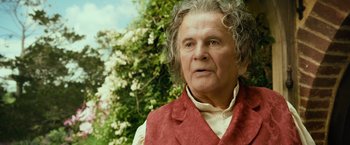 Movie still from “The Hobbit: An Unexpected Journey” (2012), directed by Peter Jackson – An older man in a red vest is looking at the camera; Close Up shot, Over the shoulder angle