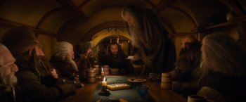 Movie still from “The Hobbit: An Unexpected Journey” (2012), directed by Peter Jackson – A group of people sitting around a table with food on it; Wide shot, Over the shoulder angle