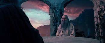 Movie still from “The Hobbit: An Unexpected Journey” (2012), directed by Peter Jackson – A man with long hair and a long beard sitting in front of a stone structure; Medium shot, Over the shoulder angle