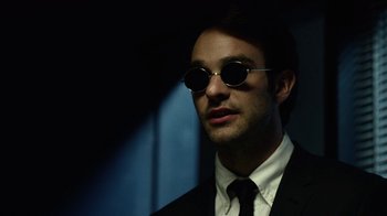 Movie still from “Daredevil” (2015), created by Drew Goddard – A man in a suit and sunglasses looking at the camera; Close Up shot, Over the shoulder angle