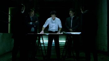 Movie still from “Daredevil” (2015), created by Drew Goddard – A group of men standing around a table; Wide shot, Overhead angle