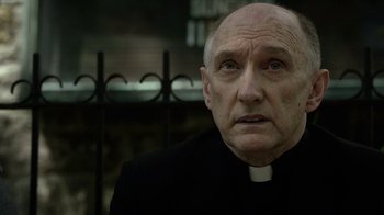 Movie still from “Daredevil” (2015), created by Drew Goddard – An older man wearing a priest's outfit; Close Up shot, Low angle