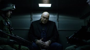 Movie still from “Daredevil” (2015), created by Drew Goddard – A man sitting on a train with his hands in his pockets; Medium shot, Low angle