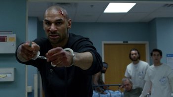 Movie still from “Daredevil” (2015), created by Drew Goddard – A man holding a pair of handcuffs in a room; Medium shot, Low angle