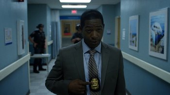 Movie still from “Daredevil” (2015), created by Drew Goddard – A man in a suit and tie holding a police badge; Medium shot, Low angle