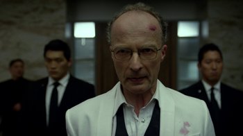 An old man with a shaved head and a white jacket