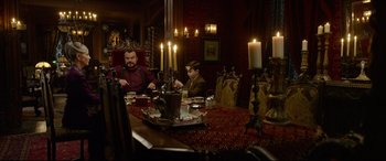 Movie still from “The House with a Clock in Its Walls” (2018), directed by Eli Roth – Two men sitting at a dinner table with candles in the background; Medium shot, Low angle