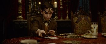 Movie still from “The House with a Clock in Its Walls” (2018), directed by Eli Roth – A young boy in a suit and goggles is playing a card game; Medium shot, Over the shoulder angle