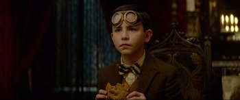 Movie still from “The House with a Clock in Its Walls” (2018), directed by Eli Roth – A young boy in a suit and goggles holding a cookie; Close Up shot, Over the shoulder angle