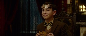 Movie still from “The House with a Clock in Its Walls” (2018), directed by Eli Roth – A young boy in a suit and tie holding a piece of food; Close Up shot, Over the shoulder angle