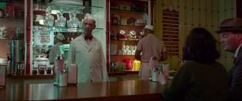 Movie still from “The House with a Clock in Its Walls” (2018), directed by Eli Roth – A man wearing a white hat standing in front of a counter; Medium shot, Over the shoulder angle