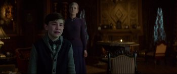 Movie still from “The House with a Clock in Its Walls” (2018), directed by Eli Roth – A boy and a woman standing in front of a fire place; Medium shot, Over the shoulder angle