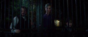 Movie still from “The House with a Clock in Its Walls” (2018), directed by Eli Roth – A woman standing behind a metal fence at night; Medium shot, Over the shoulder angle