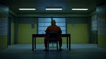 Movie still from “Daredevil” (2015), created by Drew Goddard – A man in orange is sitting at a table in front of a window; Wide shot, High angle