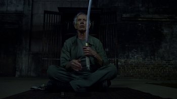 Movie still from “Daredevil” (2015), created by Drew Goddard – An old man sitting on the ground holding a sword; Medium shot, High angle