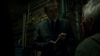 Movie still from “Daredevil” (2015), created by Drew Goddard – A man wearing a suit and tie holding a pencil; Medium shot, High angle