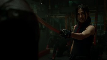 Movie still from “Daredevil” (2015), created by Drew Goddard – A woman is holding a sword in a room; Medium shot, Over the shoulder angle