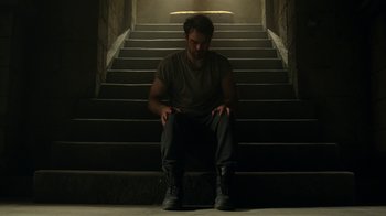 Movie still from “Daredevil” (2015), created by Drew Goddard – A man sitting on the steps of a staircase; Wide shot, High angle
