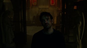 Movie still from “Daredevil” (2015), created by Drew Goddard – A man standing in a dark room looking at the camera; Close Up shot, Low angle