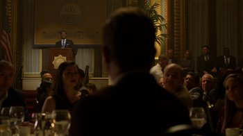 Movie still from “Daredevil” (2015), created by Drew Goddard – A group of people sitting in front of a microphone; Medium shot, Over the shoulder angle