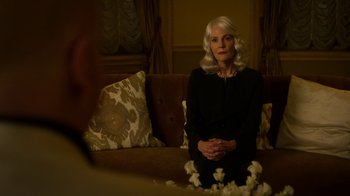 Movie still from “Daredevil” (2015), created by Drew Goddard – An older woman sitting on a brown couch; Medium shot, Over the shoulder angle