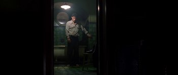 Movie still from “Dark City” (1998), directed by Alex Proyas – A man standing in a dark room with a chair; Wide shot, Low angle