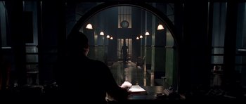 Movie still from “Dark City” (1998), directed by Alex Proyas – A man sitting at a table in front of an open door; Wide shot, Low angle