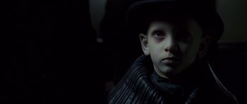 Movie still from “Dark City” (1998), directed by Alex Proyas – A young boy wearing a black hat and a black jacket; Close Up shot, High angle