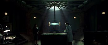 Movie still from “Dark City” (1998), directed by Alex Proyas – A man and a woman standing in front of a table in a dark room; Wide shot, High angle