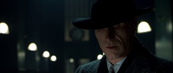 Movie still from “Dark City” (1998), directed by Alex Proyas – A person wearing a hat and a suit; Close Up shot, Over the shoulder angle