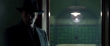 Movie still from “Dark City” (1998), directed by Alex Proyas – A man wearing a hat and a coat standing next to a window; Medium shot, Low angle