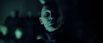 Movie still from “Dark City” (1998), directed by Alex Proyas – A man with a bald head wearing a black shirt; Close Up shot, Low angle