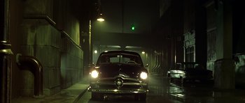 Movie still from “Dark City” (1998), directed by Alex Proyas – An old car is driving down the street at night; Wide shot, Low angle
