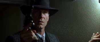 Movie still from “Dark City” (1998), directed by Alex Proyas – A man in a hat holding a gun in his hand; Close Up shot, Low angle