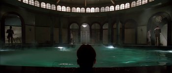 Movie still from “Dark City” (1998), directed by Alex Proyas – A man sitting in front of an indoor swimming pool at night; Extreme Wide shot, High angle