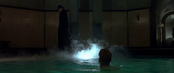 Movie still from “Dark City” (1998), directed by Alex Proyas – A person in a pool of water with smoke coming out of it; Wide shot, Over the shoulder angle