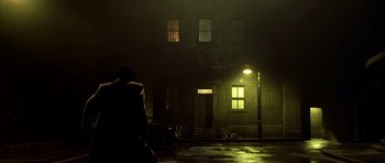 Movie still from “Dark City” (1998), directed by Alex Proyas – A person standing in front of a building at night; Wide shot, Low angle