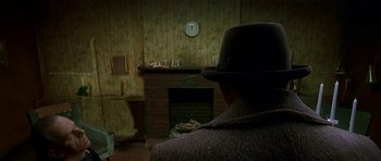 Movie still from “Dark City” (1998), directed by Alex Proyas – A man wearing a hat sitting in front of a fire place; Medium shot, Over the shoulder angle