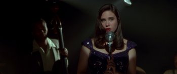 Movie still from “Dark City” (1998), directed by Alex Proyas – A woman holding a microphone in front of a microphone stand; Close Up shot, Over the shoulder angle