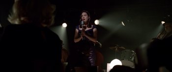 Movie still from “Dark City” (1998), directed by Alex Proyas – A woman is singing into a microphone in front of a crowd; Medium shot, Over the shoulder angle