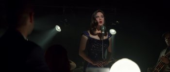 Movie still from “Dark City” (1998), directed by Alex Proyas – A woman in a blue dress is singing into a microphone; Medium shot, Over the shoulder angle