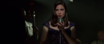 Movie still from “Dark City” (1998), directed by Alex Proyas – A beautiful young lady holding a microphone and singing; Close Up shot, Over the shoulder angle