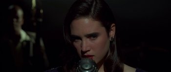 Movie still from “Dark City” (1998), directed by Alex Proyas – A woman with dark hair is holding a microphone up to her face; Close Up shot, High angle