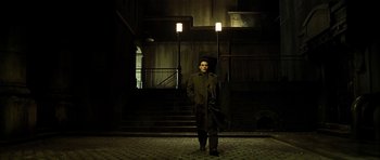 Movie still from “Dark City” (1998), directed by Alex Proyas – A man standing in front of some stairs at night; Wide shot, Low angle