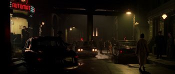 Movie still from “Dark City” (1998), directed by Alex Proyas – A group of people standing around parked cars at night; Wide shot, High angle