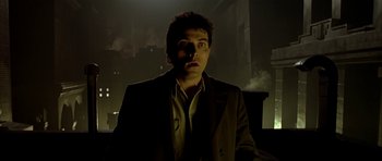 Movie still from “Dark City” (1998), directed by Alex Proyas – A man standing in a dark room with smoke coming out of a window; Medium shot, Low angle