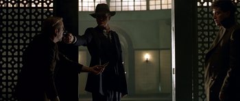 Movie still from “Dark City” (1998), directed by Alex Proyas – A man in a suit and a hat holding a pair of scissors; Medium shot, Low angle