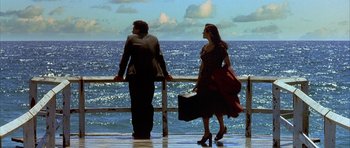 Movie still from “Dark City” (1998), directed by Alex Proyas – A man and a woman standing next to a railing looking out at the ocean; Wide shot, Low angle
