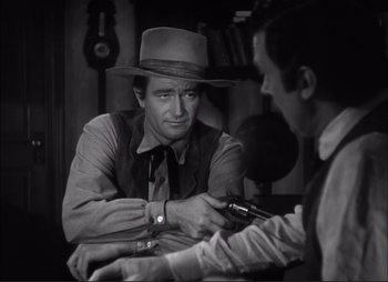 Movie still from “Dark Command” (1940), directed by Raoul Walsh – A man wearing a hat is holding a cell phone; Medium shot, Over the shoulder angle