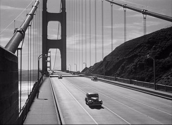 Movie still from “Dark Passage” (1947), directed by Delmer Daves – A black and white photo of a car on a bridge; Extreme Wide shot, High angle